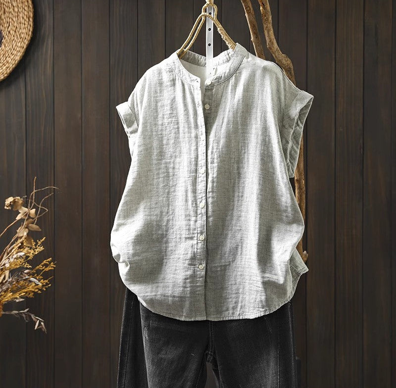 Light gray sleeveless shirt hanging on a wooden wall with dried plants.